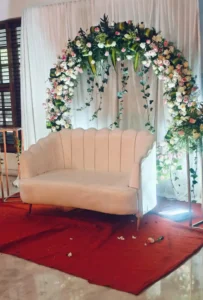 Floral setup by HKGN Tent House & Decoration in Hyderabad: a white loveseat before an arch of white and pink blooms and greenery, set on a red carpet. - HKGN Tent House & Decoration - Tent Hire in Hyderabad Floral setup by HKGN Tent House & Decoration in Hyderabad: a white loveseat before an arch of white and pink blooms and greenery, set on a red carpet.