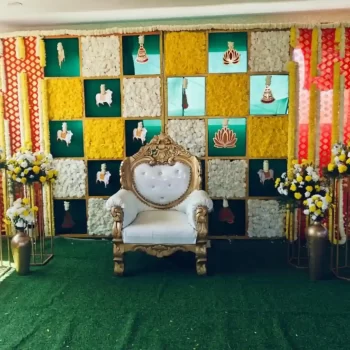 Graceful event setup by HKGN Tent House & Decoration, Hyderabad, with a royal carved chair framed by neatly arranged flowers and a colourful, artistic backdrop. Well suited to weddings and special occasions. Tent hire services in Hyderabad.